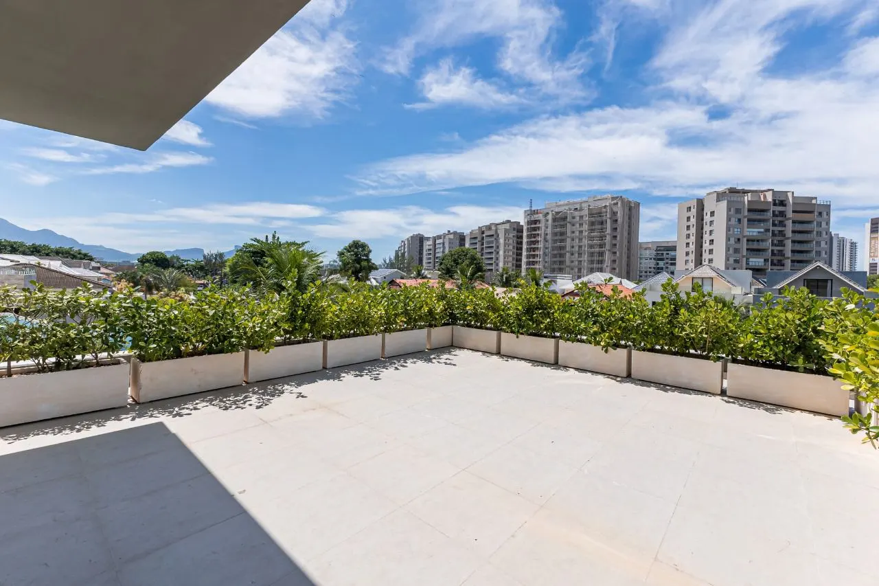 Terraço descoberto com floreiras e vista para os prédios e montanhas da Barra