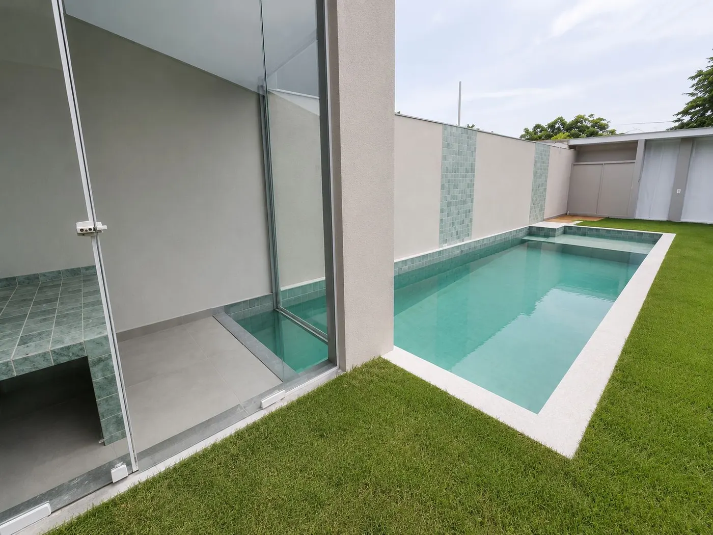 Piscina com sauna envidraçada ao lado, em quintal gramado