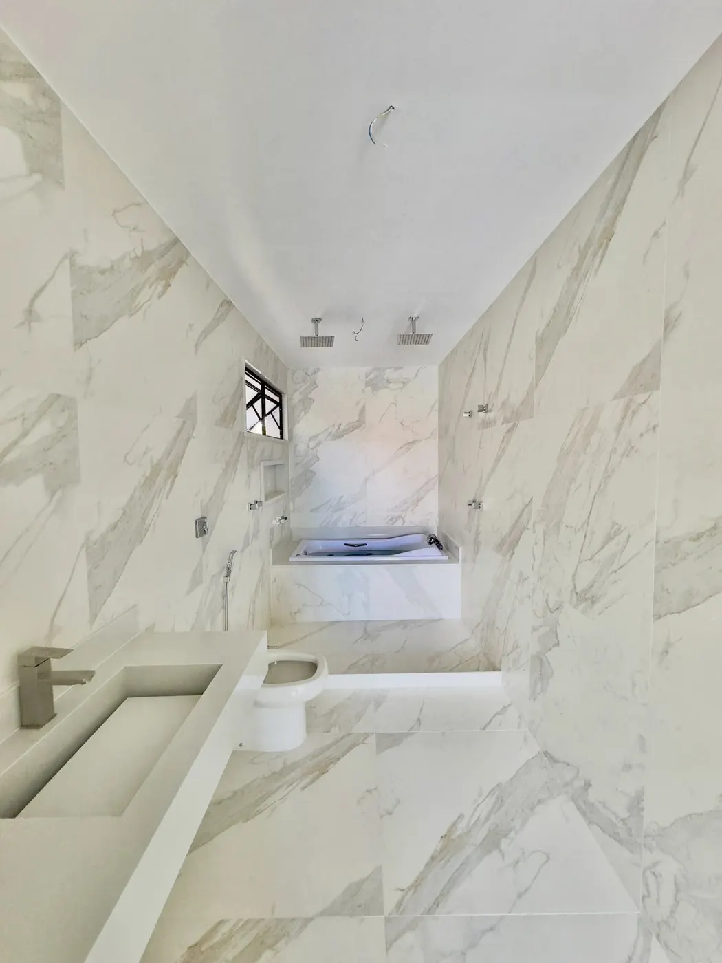 Banheiro de suíte revestido em porcelanato marmorizado, com bancada esculpida