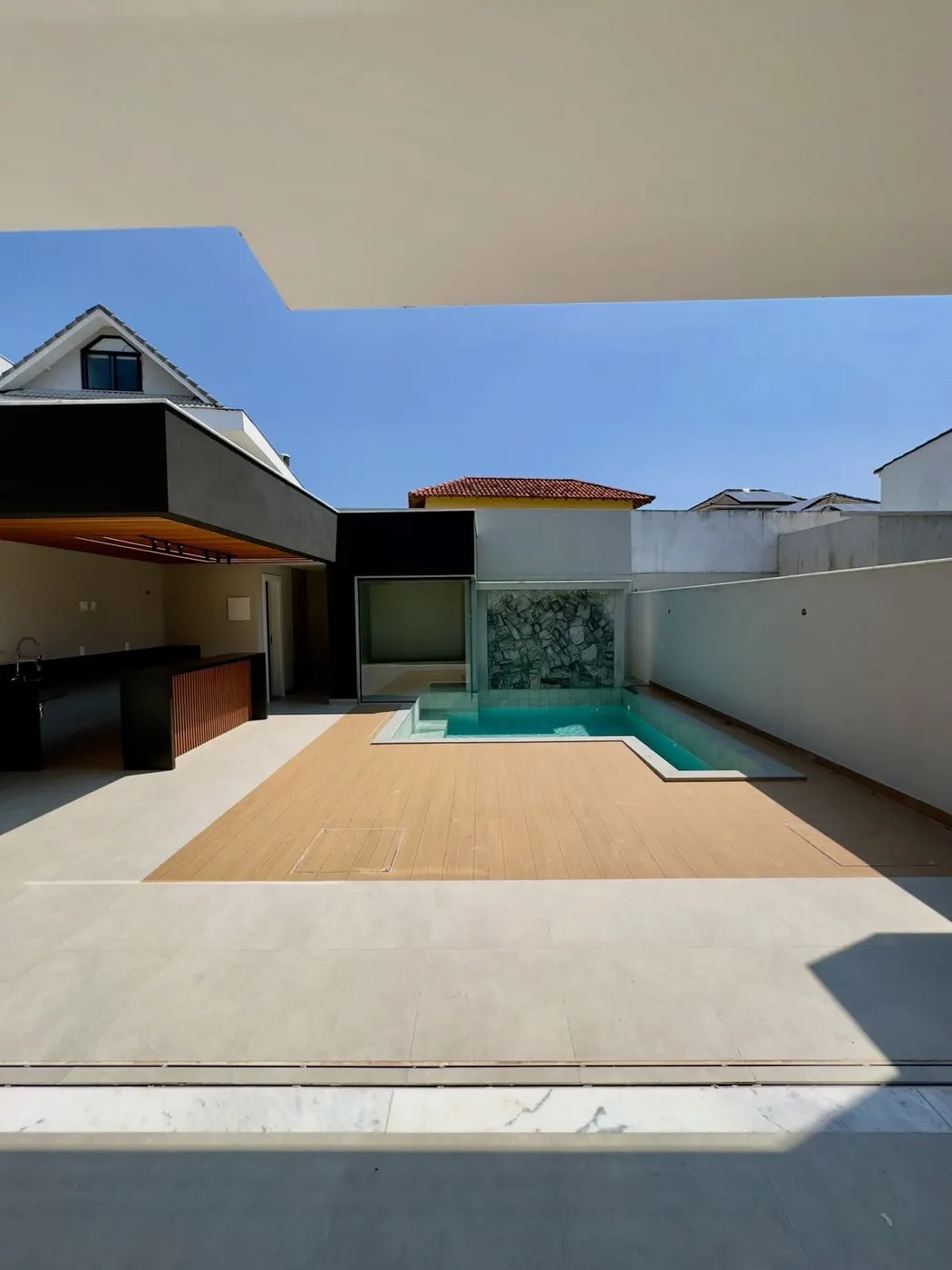 Área externa com piscina, deck de madeira e espaço gourmet coberto